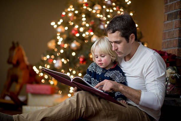 Father is reading his little boy a book on Christmas A father is reading his little boy a book on Christmas Eve. christmas story telling stock pictures, royalty-free photos & images