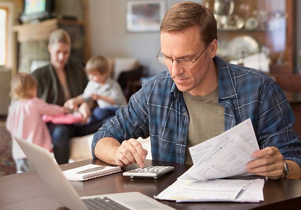 father paying bills with family behind him - geldstress stockfoto's en -beelden