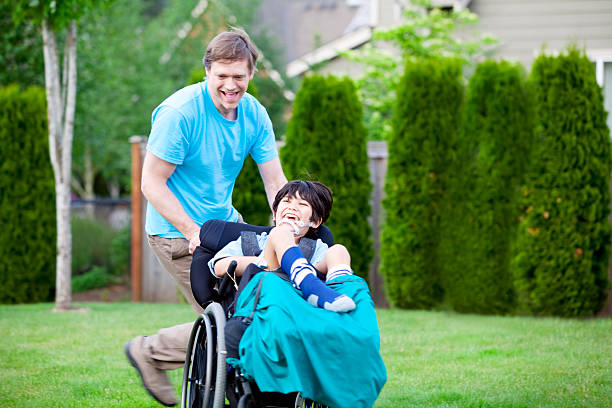 Father racing around park with disabled son in wheelchair stock photo