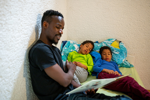 Father reading a story to his two little sons in a bedroom.