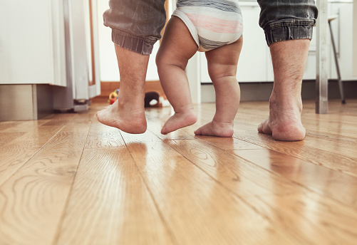 First steps of a child with his father's help. Both barefoot on hardwood floor. What a joy.....