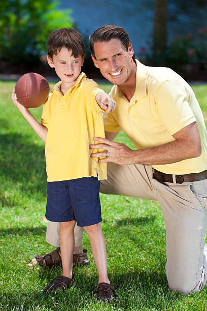 A father teaching his son how to play American football outside in...
