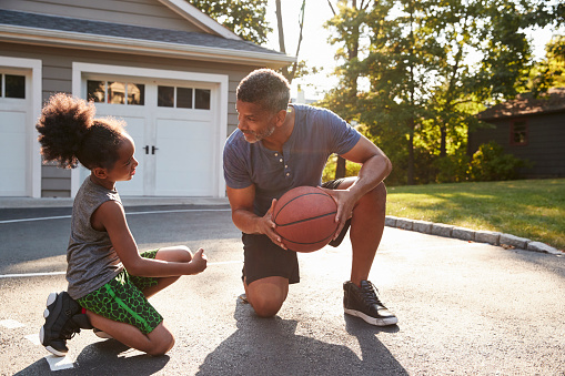 Father Teaching Son How To Play Basketball On Driveway At