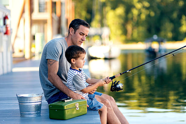 father teaching son how to use a fishing pole - havenmeester stockfoto's en -beelden