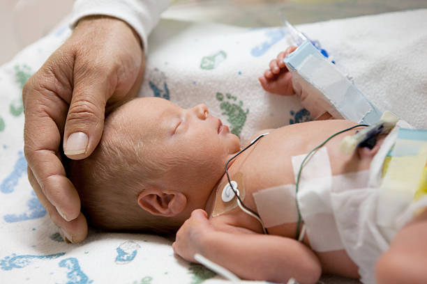 father touching head of a premature baby in incubator stock photo
