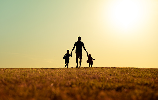 Father walking with his kids in the park at sunset.