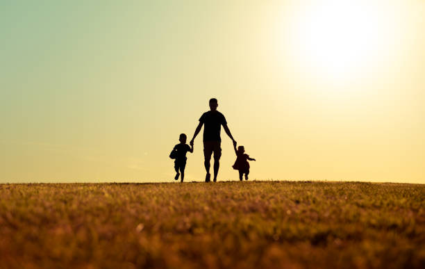 Father walking with son and daughter in park at sunset. stock photo