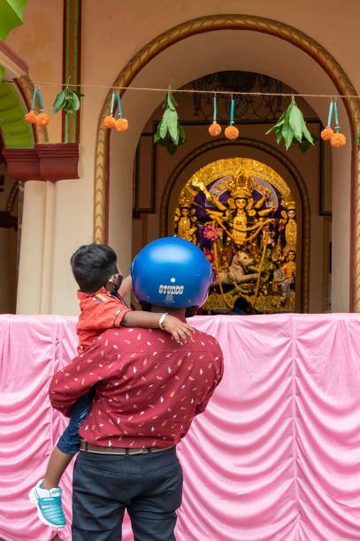 Father with helmet on, showing Goddess Durga to his child, Durga inside old age decorated home. Durga Puja, biggest festival of Hinduism, UNESCO heritage of humanity. stock photo