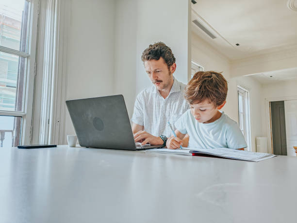 Father working while his sons do their homework stock photo