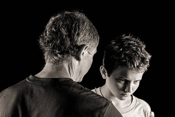 Father-son serious talk Moody monochrome portrait of man and his 12-year old son having a difficult time together chiaroscuro stock pictures, royalty-free photos & images