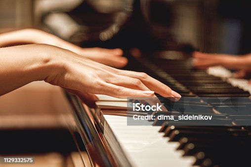 istock Favorite classical music...Close up view of gentle female hands playing a melody on piano while taking piano lessons 1129332575