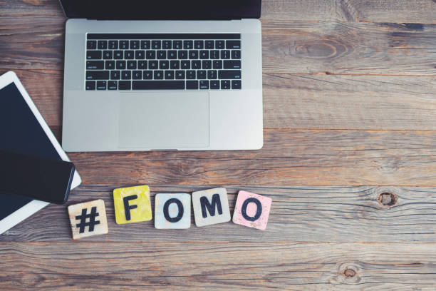 FOMO, Fear OF Missing Out. Laptop, digital tablet and mobile phone with a hashtag and the letters FOMO beside them. FOMO, Fear OF Missing Out. Laptop, digital tablet and mobile phone with a hashtag and the letters FOMO beside them. They are on a wooden background with copy space. fomo photos stock pictures, royalty-free photos & images