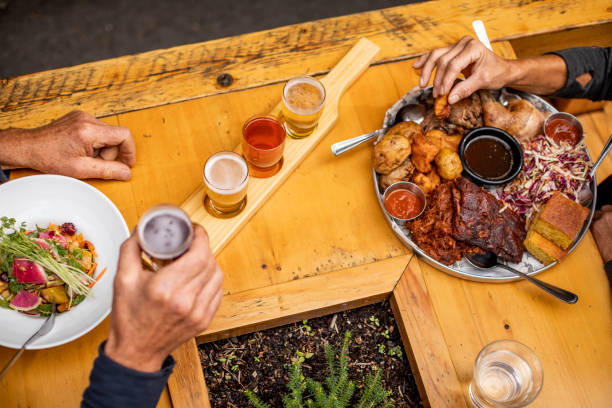 BBQ feast and vegan salad on table. High angle view of people eating bbq meat and drinking beer in a pub. comfort food stock pictures, royalty-free photos & images
