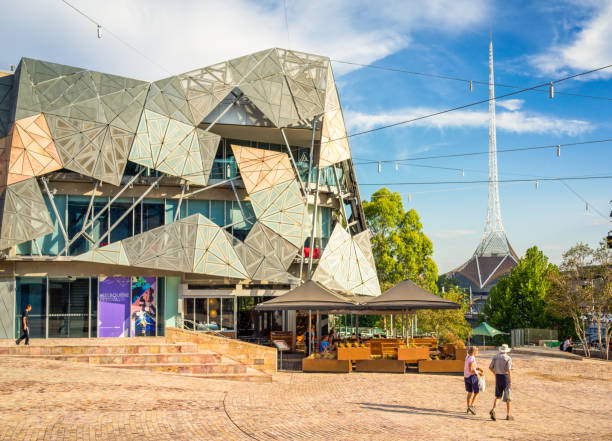 Federation Square in central Melbourne Melbourne, Australia - People in Federation Square in Melbourne's city centre on a sunny and hot day, with the spire of the Melbourne Arts Centre to the right. federation square stock pictures, royalty-free photos & images