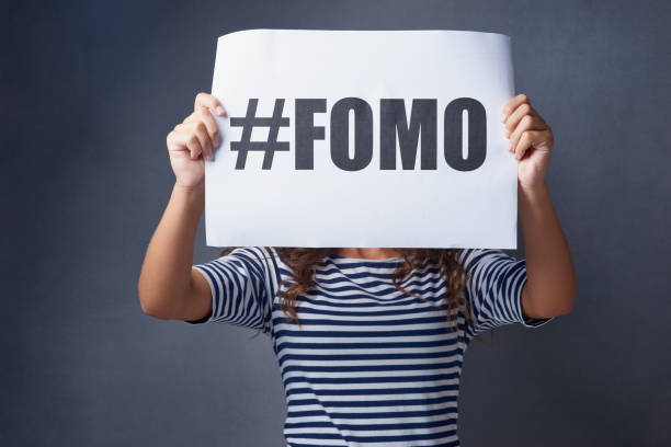 I feel so excluded Studio shot of a young woman holding a sign with #FOMO printed on it against a gray background fomo photos stock pictures, royalty-free photos & images