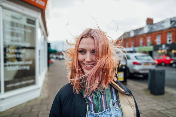 Feeling Carefree Woman standing outdoors looking away from the camera while her hair blows in the wind. pink hair stock pictures, royalty-free photos & images