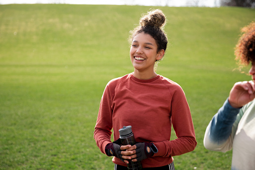Two women are working out in their community to get exercise and spend quality time together. They are currently taking a break, talking while holding water bottles.