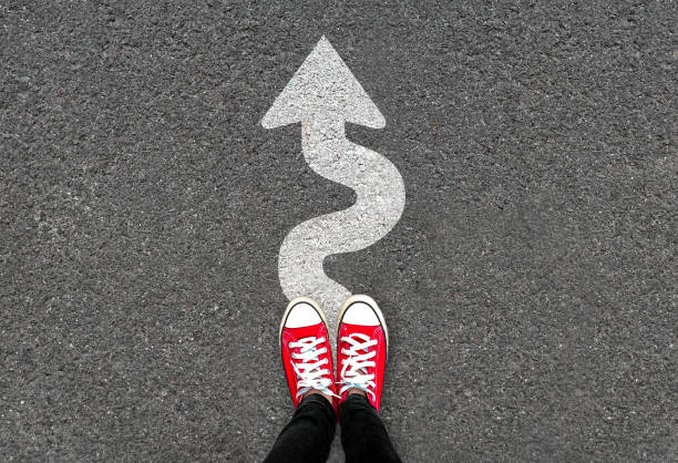 Feet and white arrow sign go straight on road background. Top view of woman. Forward movement and motivation idea concept. Feet and white arrow sign go straight on road background. Top view of woman. Forward movement and motivation idea concept. Selfie of foot and legs in red sneaker shoes on pavement floor from above. on the move stock pictures, royalty-free photos & images