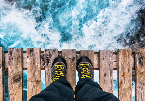 feet in boots on the edge of an old wooden bridge stock photo