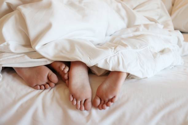 feet of two people under a blanket on the bed feet of two people under a blanket on the bed asian girls feet stock pictures, royalty-free photos & images