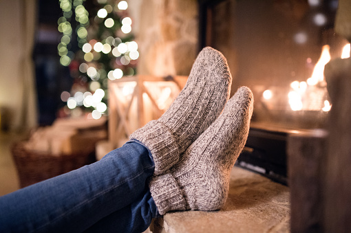 Feet of unrecognizable woman in woollen socks by the Christmas fireplace. Winter and Christmas holidays concept.