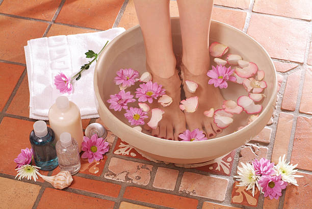 Feet stood in bowl of water with flowers next to lotions stock photo