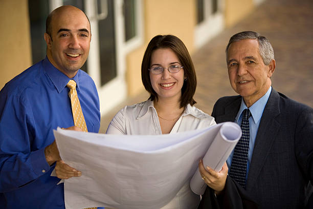 Female architect with two males holding architectural plans stock photo