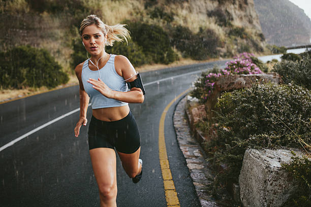 Female athlete running outdoors on highway Female athlete running outdoors on highway. Beautiful young woman training running on a rainy day. endurance stock pictures, royalty-free photos & images