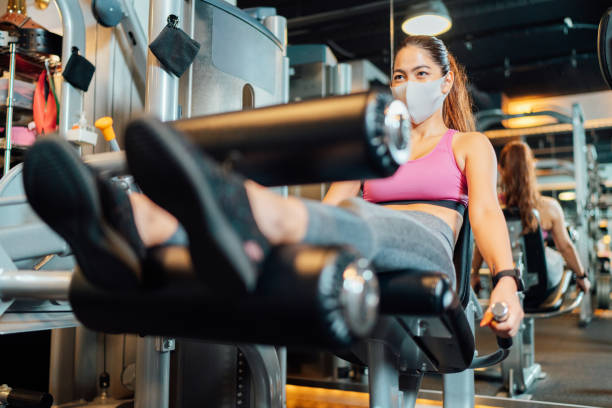 Female athlete training her legs in gym while wearing protective face mask A female athlete is training her legs in a gym while wearing a protective face mask. exercise machine stock pictures, royalty-free photos & images