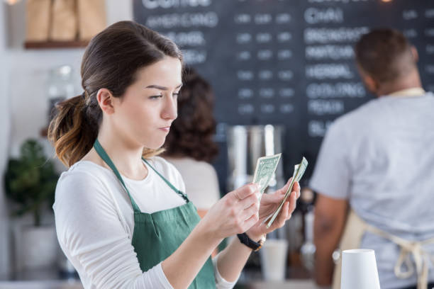 Female barista is disappointed with her tips Young female barista has a disappointed expression on her face as she counts her tips at the end of the day. tipping in restaurants stock pictures, royalty-free photos & images