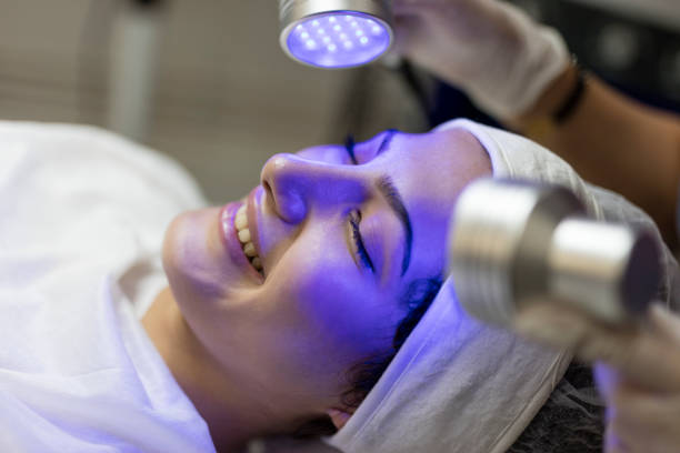 Female Beautician Doing Blue Light Therapy On face of pretty young woman Skin Cosmetology. Woman beautician Doing Blue Light Therapy On face of pretty young woman beauty treatment stock pictures, royalty-free photos & images