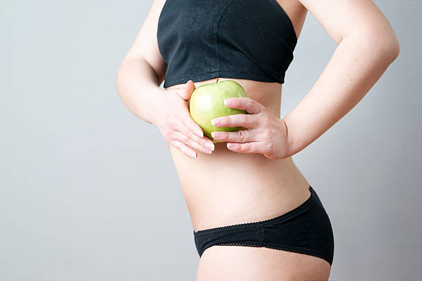 Female body with green apple on gray background. Weight loss, diet