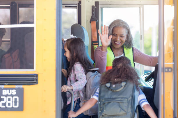 Female bus driver high-fives children boarding bus As her riders board the school bus, a female bus driver high-fives them from the driver's seat. school buses stock pictures, royalty-free photos & images