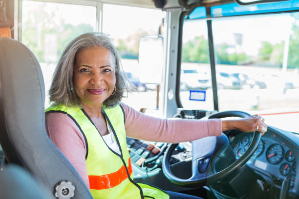 Female bus driver looks at camera confidently A senior female bus driver turns to look at the camera from the driver's seat of her school bus. She has one hand on the steering wheel. school bus driver stock pictures, royalty-free photos & images