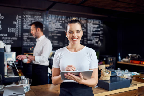 Female cafe manager standing with digital tablet with employee in background stock photo