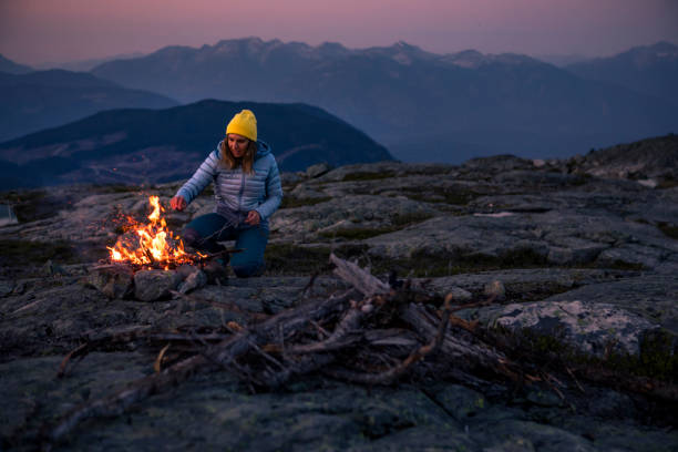 Female camper making bonfire on top of mountain. stock photo