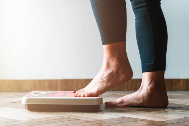 体重計に乗る女性のチェックキログラム - セルフケアと身体陽性の概念 - 左に暖かいフレア - ダイエット 写真 ストックフォトと画像