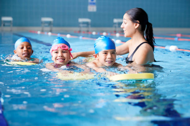 entraîneur féminin dans l'eau donnant le groupe des enfants natation de leçon dans la piscine intérieure - natation photos et images de collection
