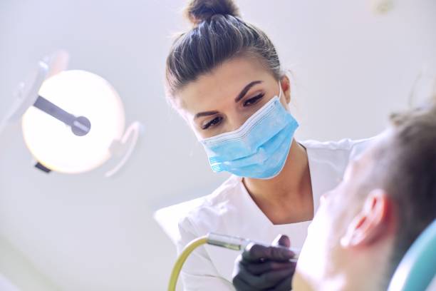 vrouwelijke tandarts die tanden aan patiënt behandelt, jonge mens in stoel bij tandkliniek - tandarts stockfoto's en -beelden