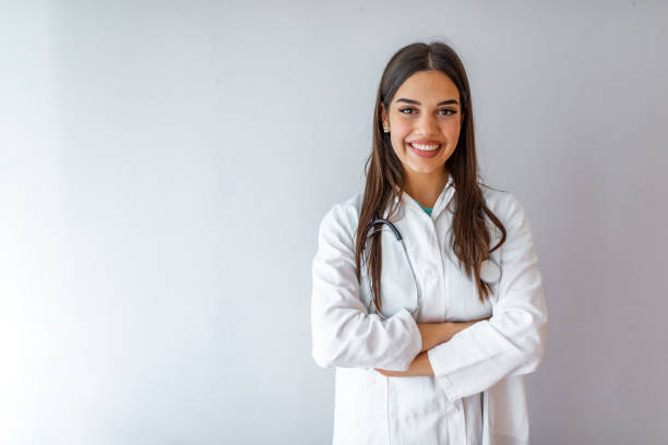 Female doctor at the hospitalCheerful happy doctor with crossed hands on grey background. Smiling medical woman doctor. Isolated over grey background. Cheerful happy doctor with crossed hands on grey background. Portrait of glad smiling doctor in white uniform standing with crossed hands on gray background lab coat stock pictures, royalty-free photos & images