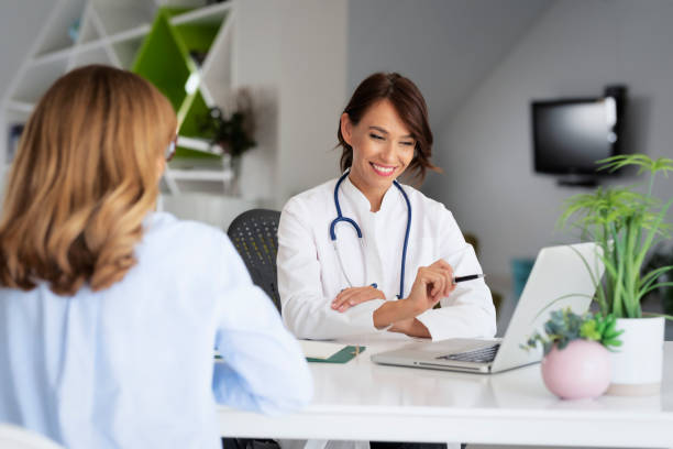 Female doctor consulting her patient while sitting at desk in doctor's office stock photo