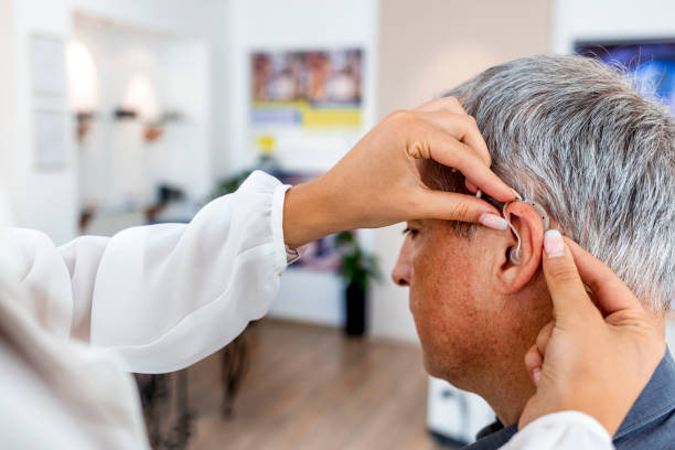 Female doctor fitting a male patient with a hearing aid stock photo