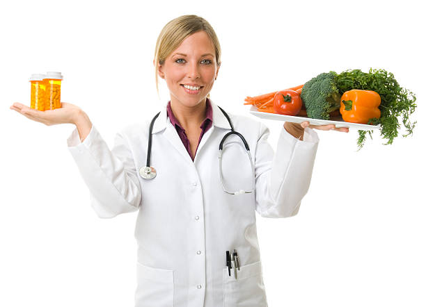 Female doctor holding plate of vegetables and vials of pills stock photo