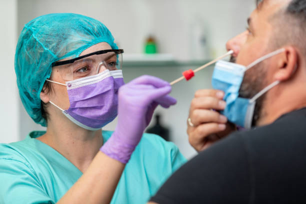 doctora mujer en ropa de trabajo protectora tomando prueba de hisopo nasal de hombre adulto medio - covid test fotografías e imágenes de stock