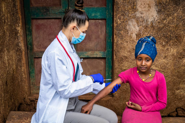 Female doctor is doing an injection to young African girl in small village, East Africa stock photo