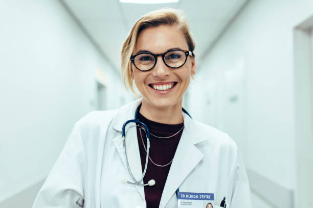 Female doctor standing in hospital corridor Portrait of happy young female doctor standing in hospital corridor. Caucasian woman working in healthcare center. female doctor stock pictures, royalty-free photos & images