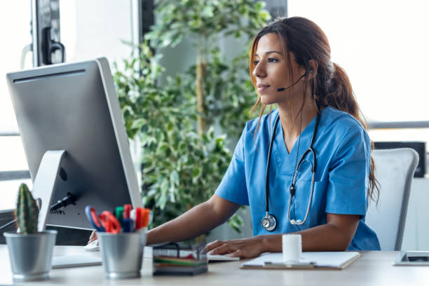 Female doctor talking with earphone while explaining medical treatment to patient through a video call with computer in the consultation. stock photo