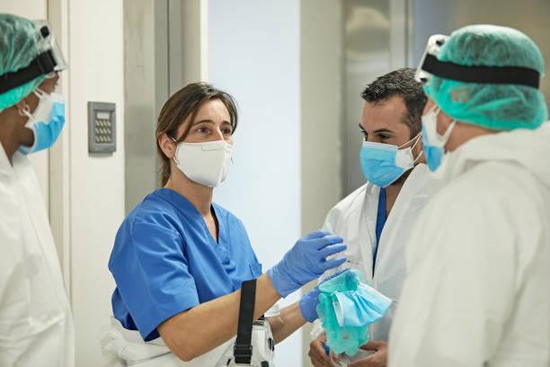 Female Doctor Talking with Medical Team in Protective Wear Mature Caucasian female medical professional standing with hospital coworkers dressed in varying degrees of protective wear. frontline worker stock pictures, royalty-free photos & images