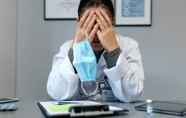 Female doctor with pandemic fatigue covering her face stock photo