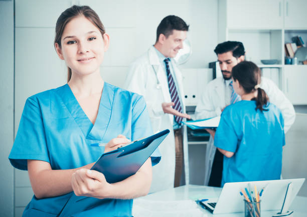 Female doctor writing notes on clipboard Smiling young female doctor writing notes on clipboard in clinic assistant stock pictures, royalty-free photos & images